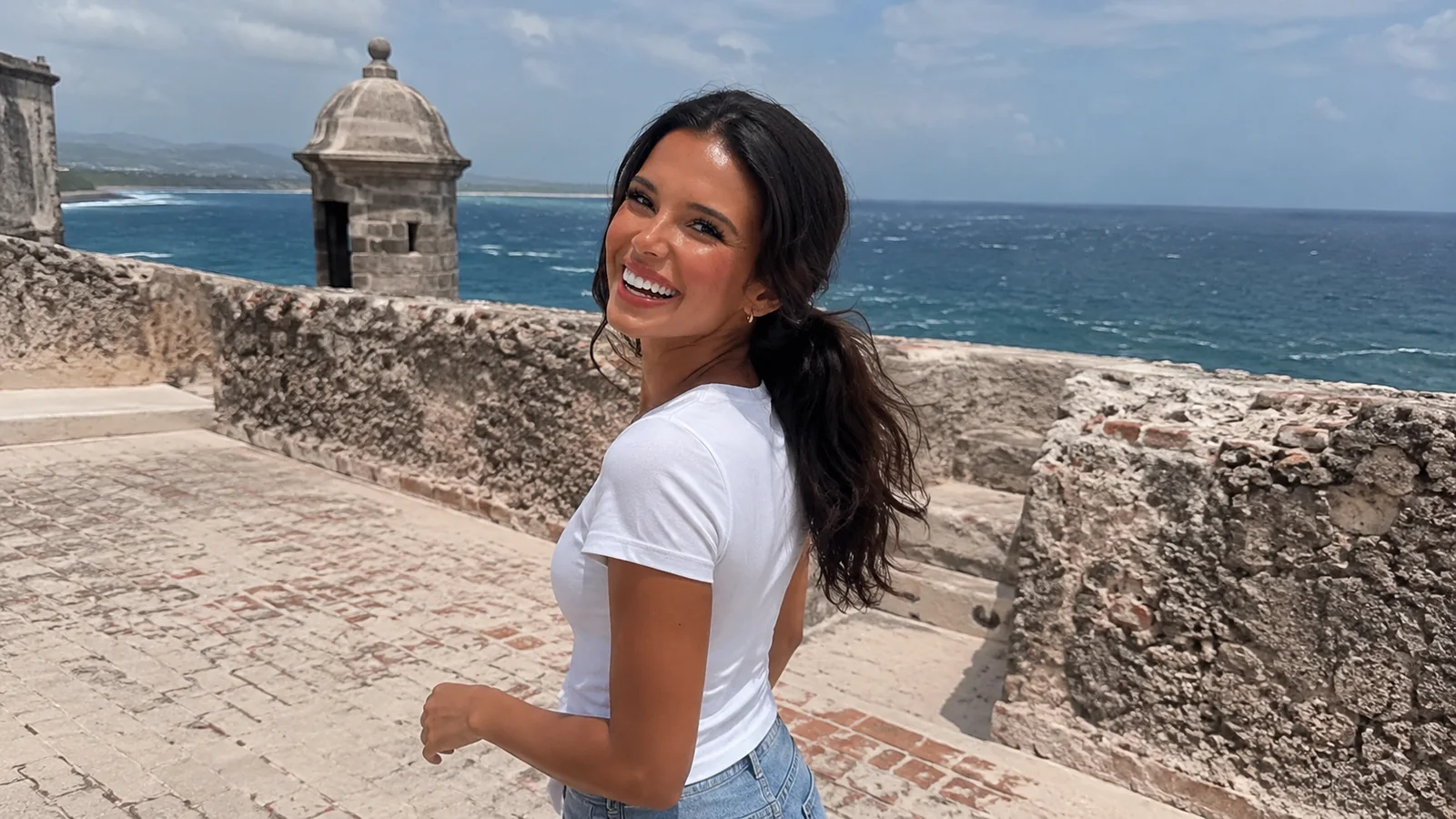 Woman walking along a stone coastal fort overlooking the sea.