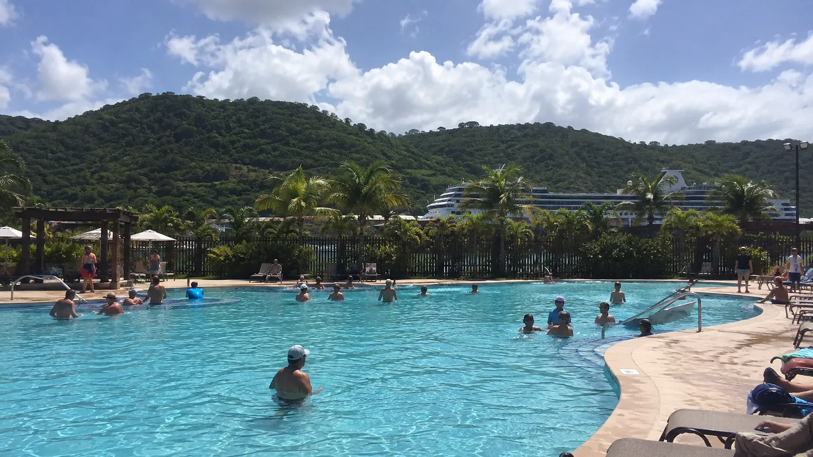Cruise-port swimming pool surrounded by palms and green hills.
