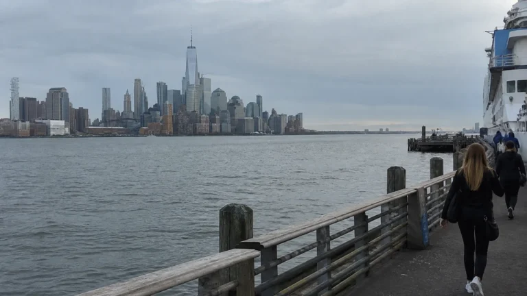 Passengers walking along a cruise pier with Manhattan's skyline across the water.