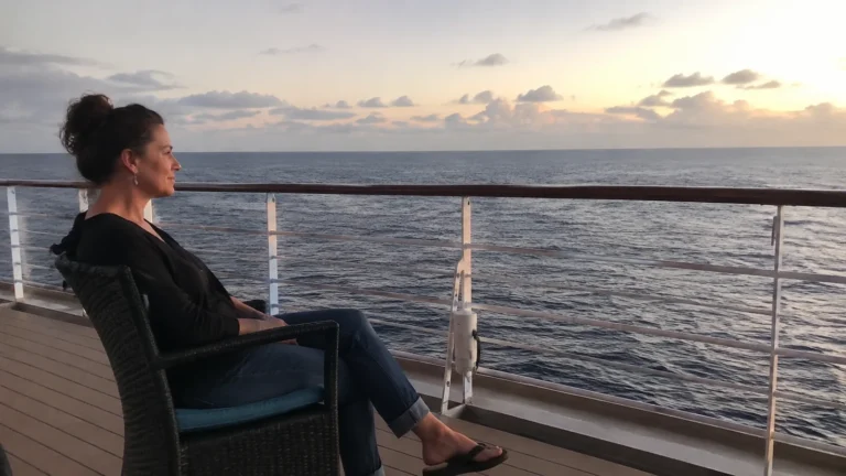 Woman relaxing in a deck chair facing the ocean at sunset.