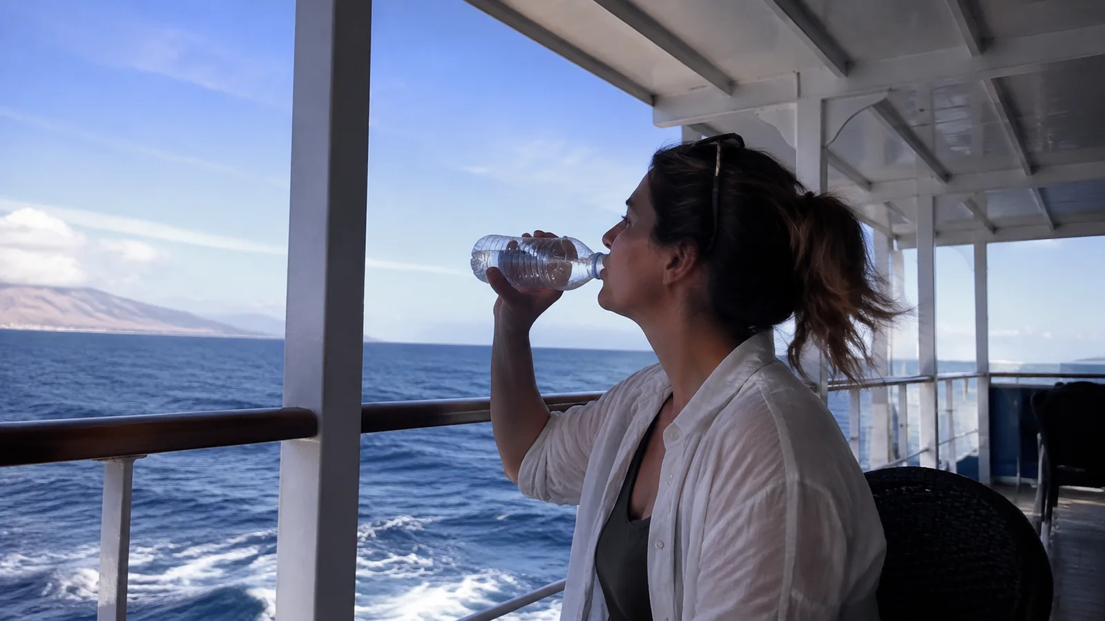 Woman drinking from a water bottle on an outdoor ship deck.