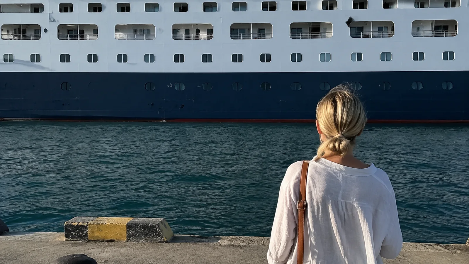Woman standing on a pier beside the hull of a large ship.