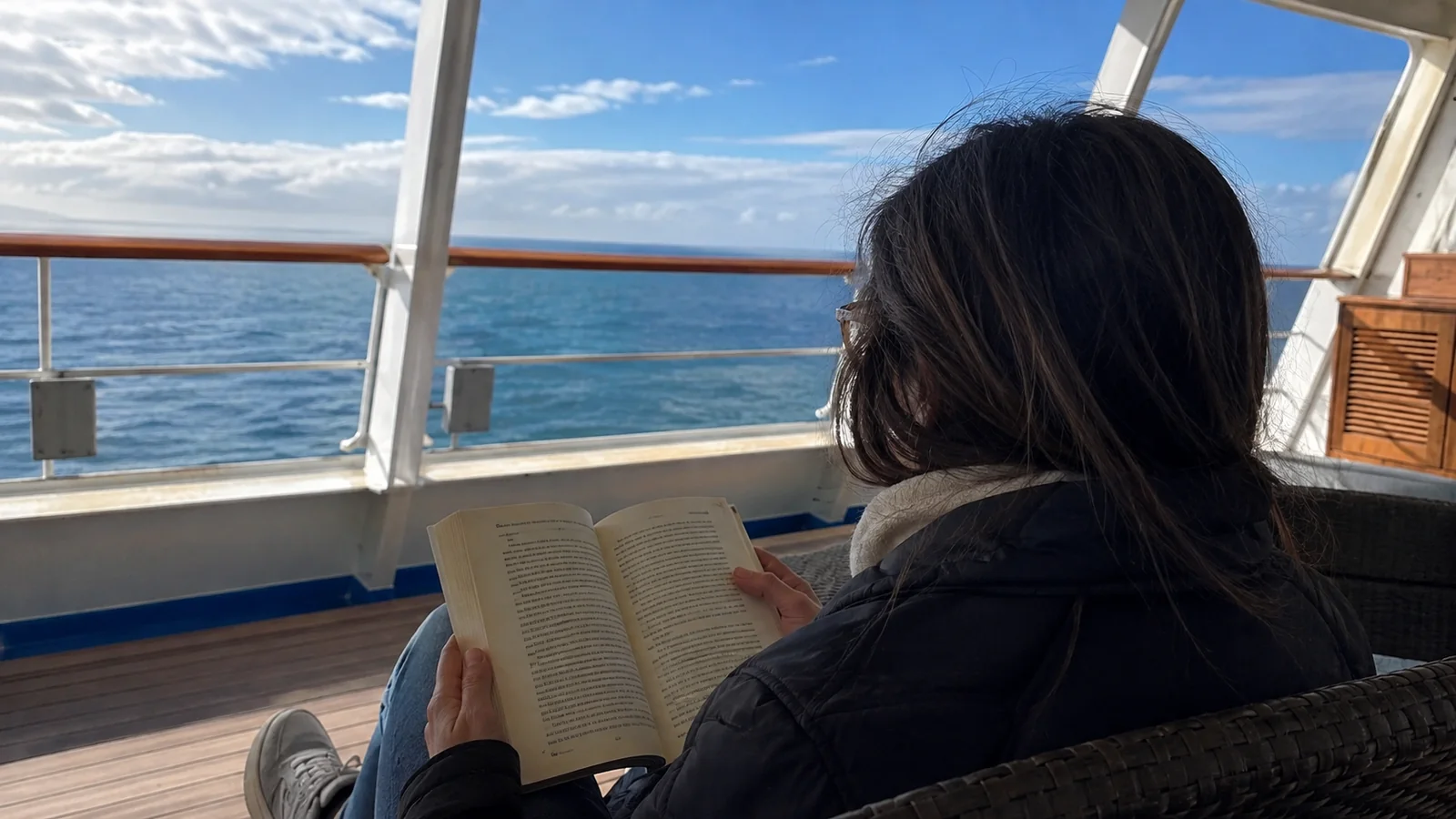 Woman reading a book in a deck chair beside the sea.