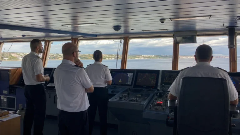 Uniformed officers monitoring controls on a ship's bridge.