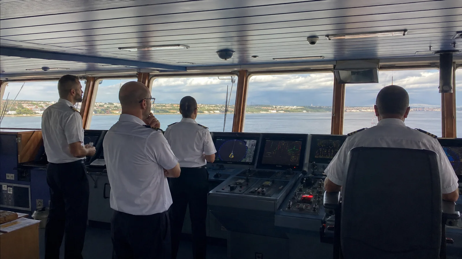 Uniformed officers monitoring controls on a ship's bridge.