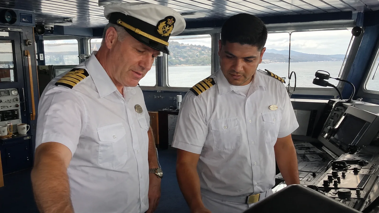 Two deck officers reviewing a control console on the bridge.
