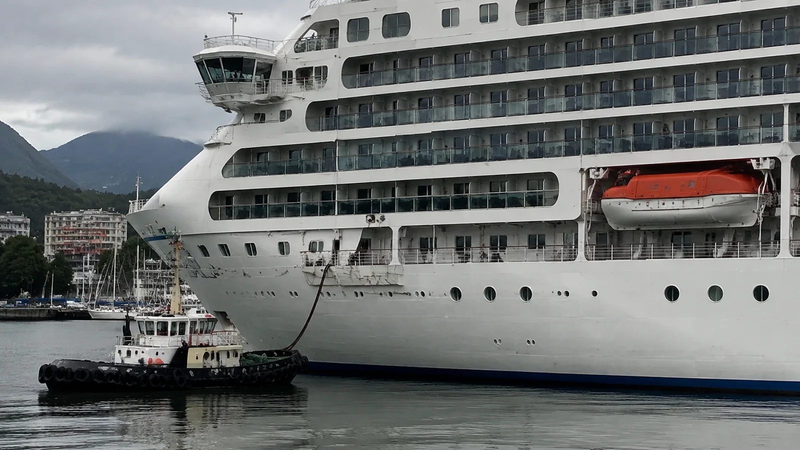 Tugboat alongside a large cruise ship near its forward decks.