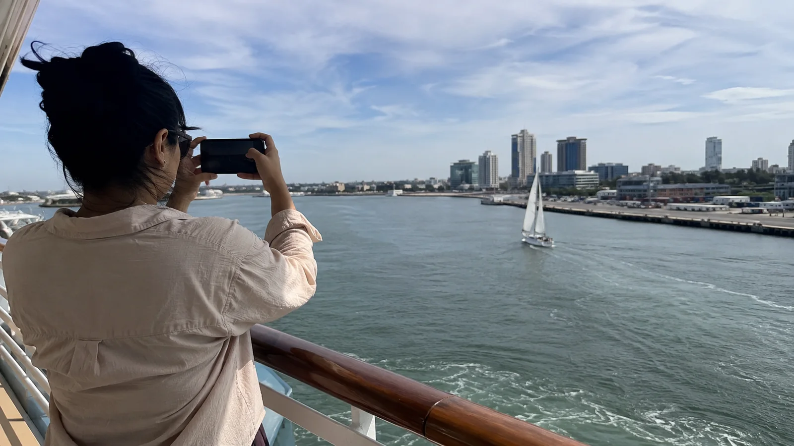 Woman photographing a harbor skyline from a ship railing.