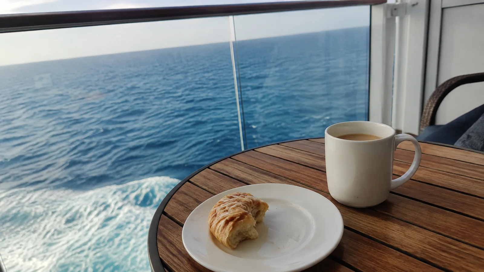 Coffee and a pastry on a balcony table overlooking the ocean.