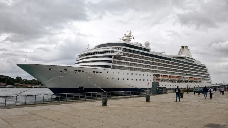 Large modern cruise ship docked beside a broad waterfront promenade.