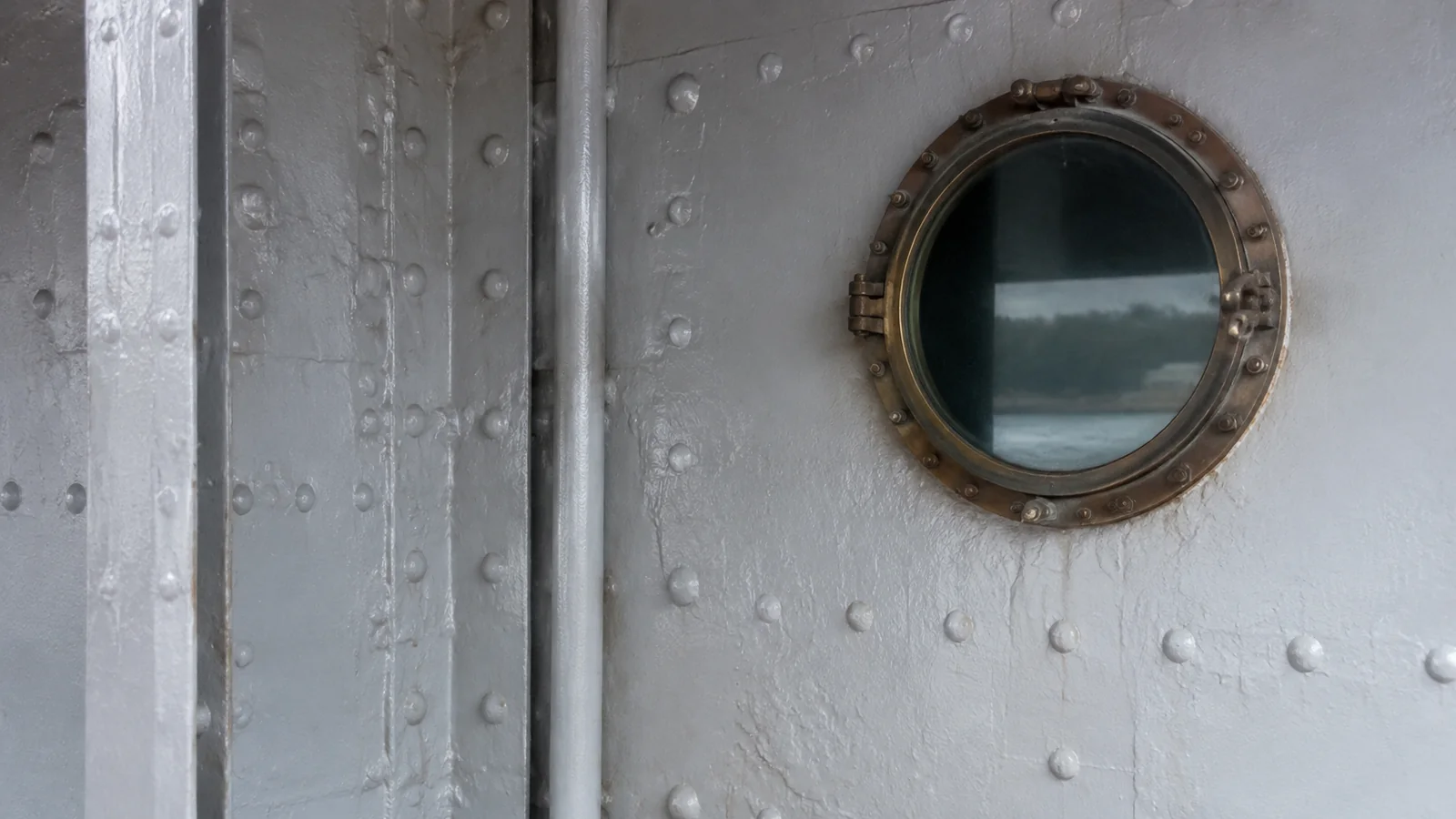 Round porthole set into a white riveted metal bulkhead.