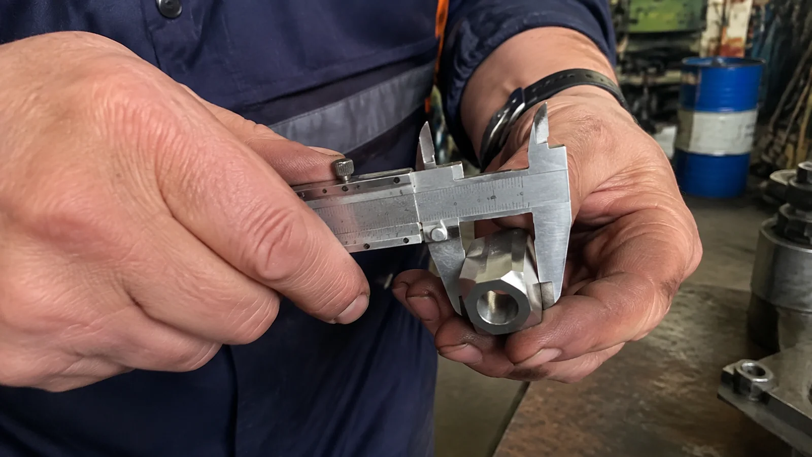 Hands measuring a metal component with calipers.