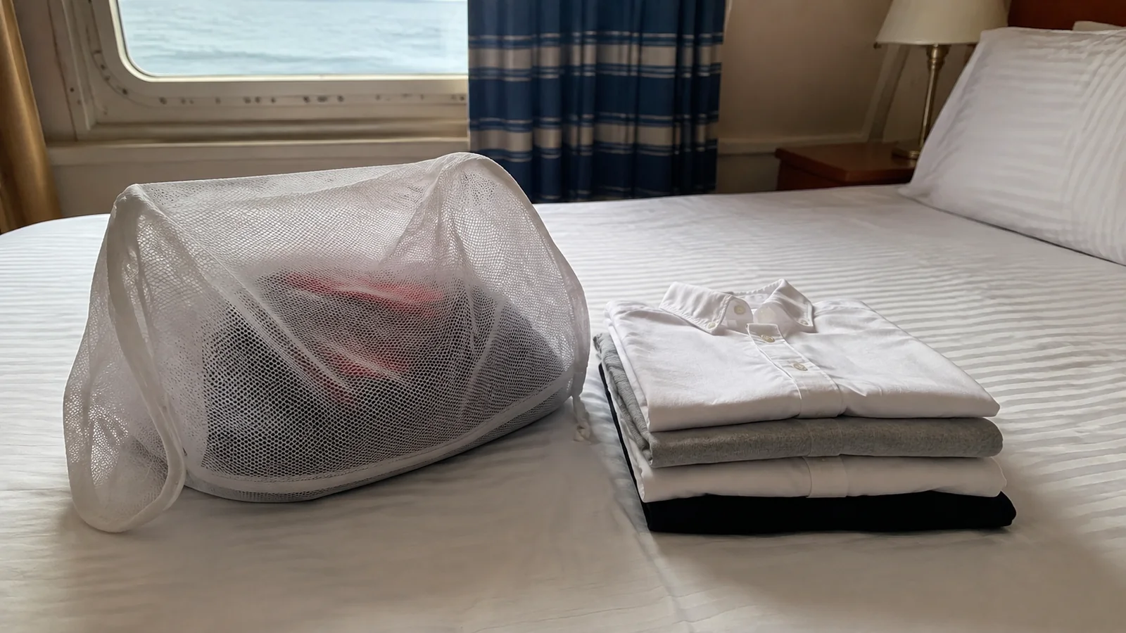 Mesh laundry bag and folded clothing rest on a stateroom bed.