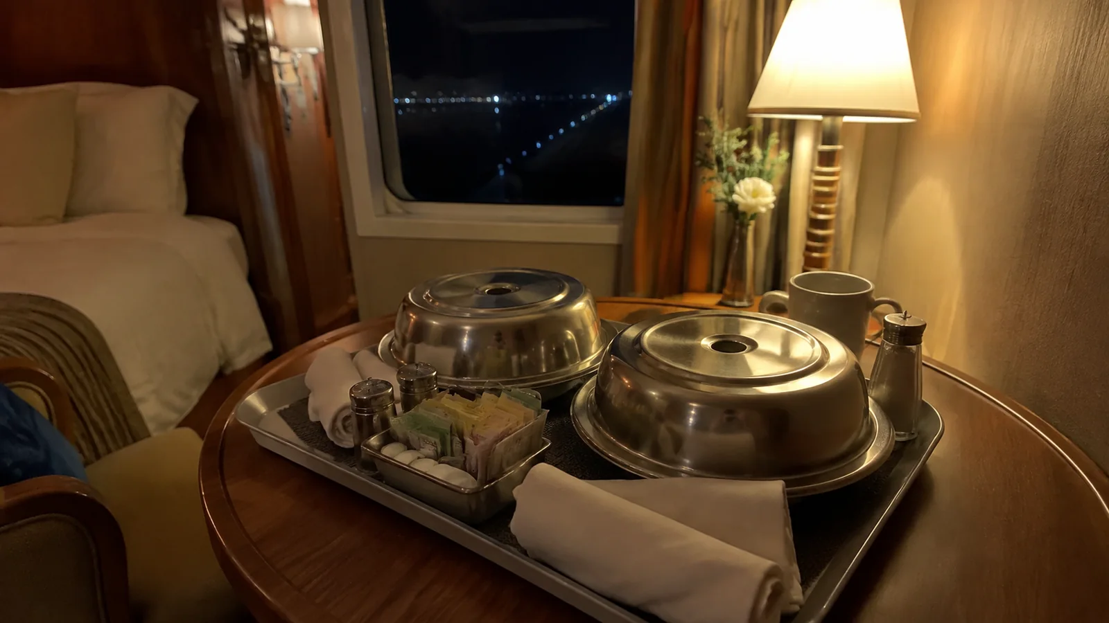 Covered meal trays sit beneath a lamp inside a stateroom.