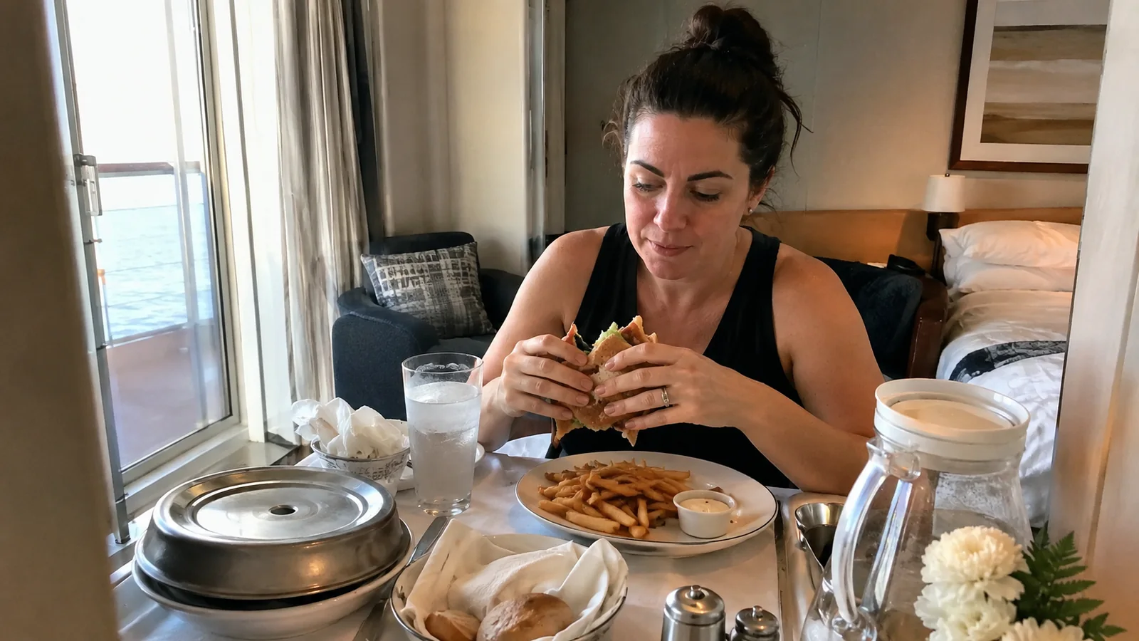 Woman eats a sandwich at a small table in her stateroom.