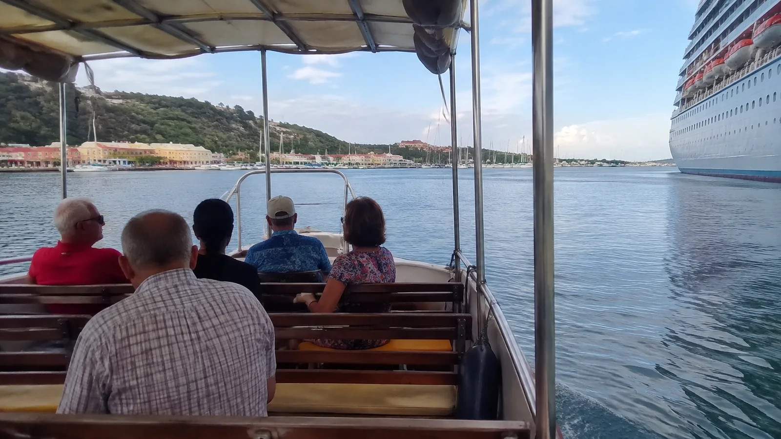 Passengers sit in a covered tender boat near a cruise ship.