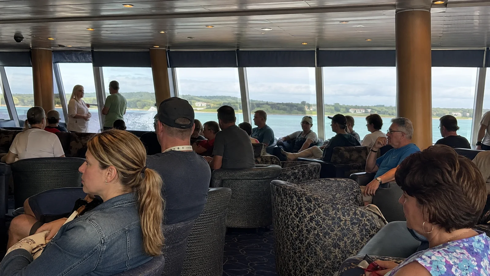 Passengers wait in a lounge with large windows facing the harbor.