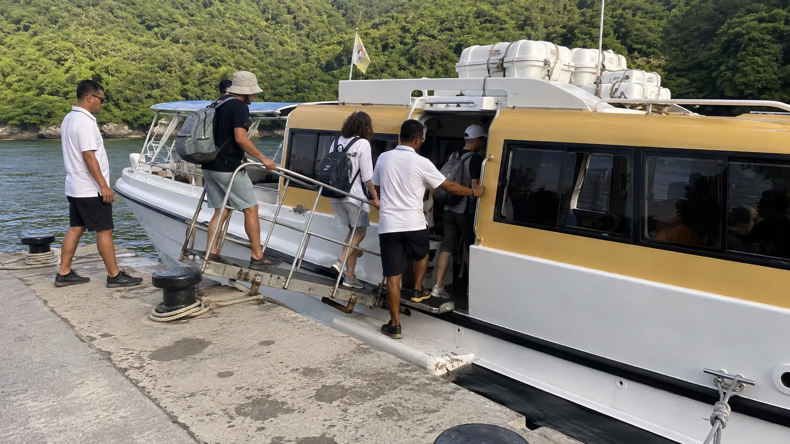 Passengers board a small boat with assistance from dockside crew.