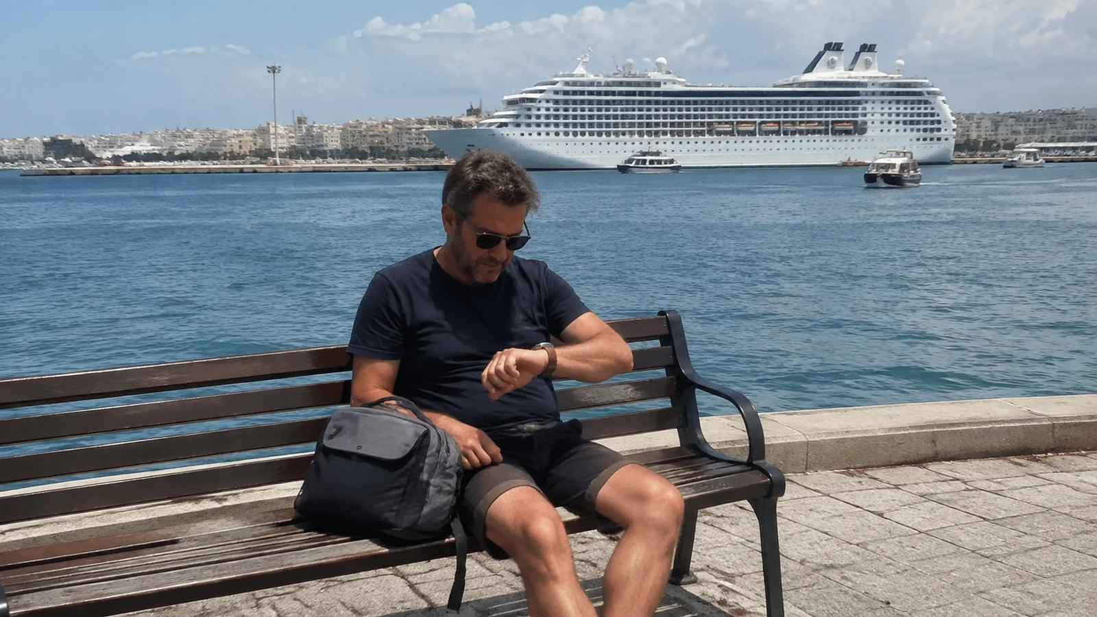 Man checks his watch while seated on a waterfront bench.