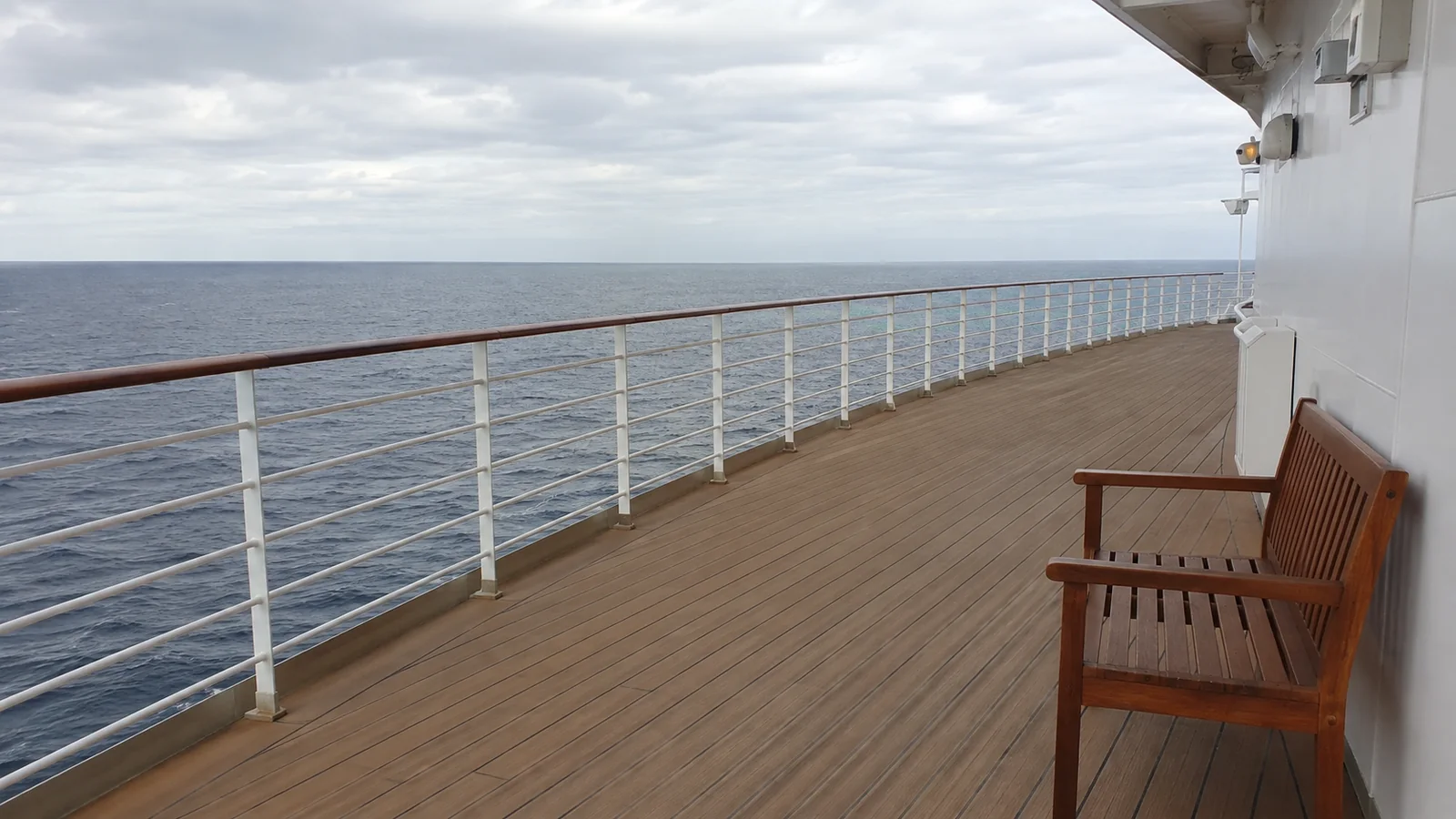 Empty wooden promenade with a bench beside an ocean-facing railing.