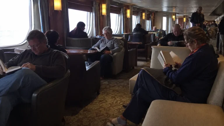 Adults reading quietly in an ocean-view ship lounge.