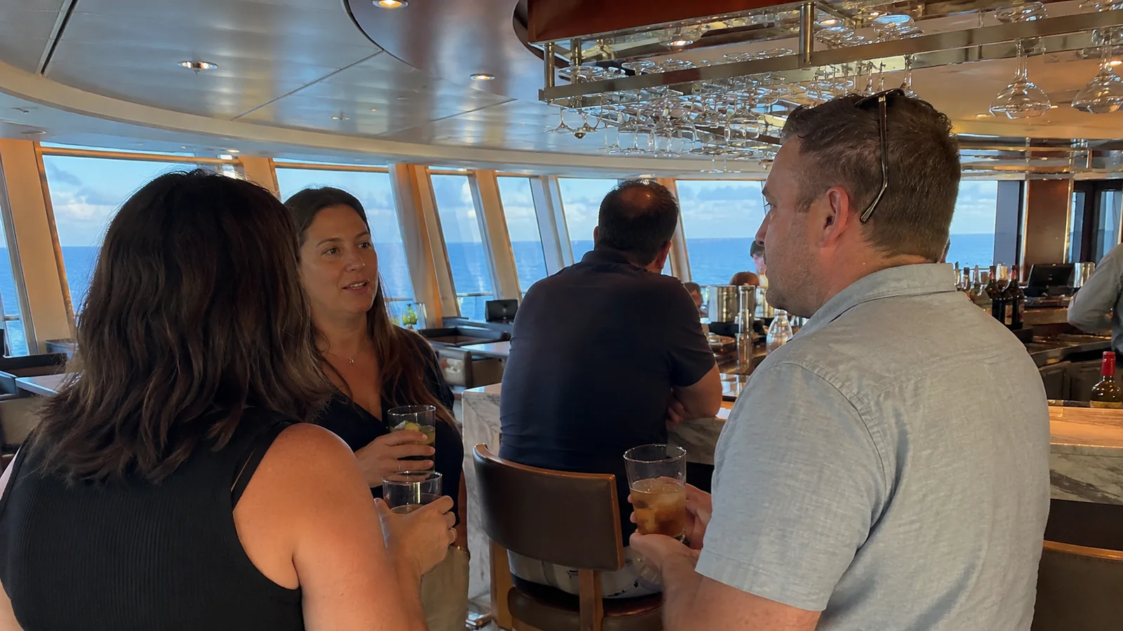 Passengers chatting over drinks at an ocean-view ship bar.
