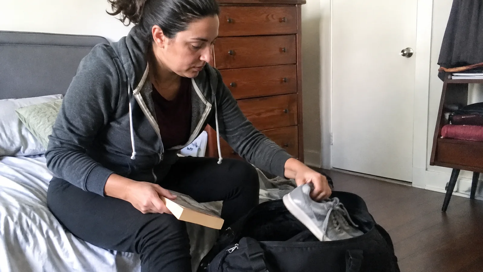 Woman packing a book and clothing into a travel bag.
