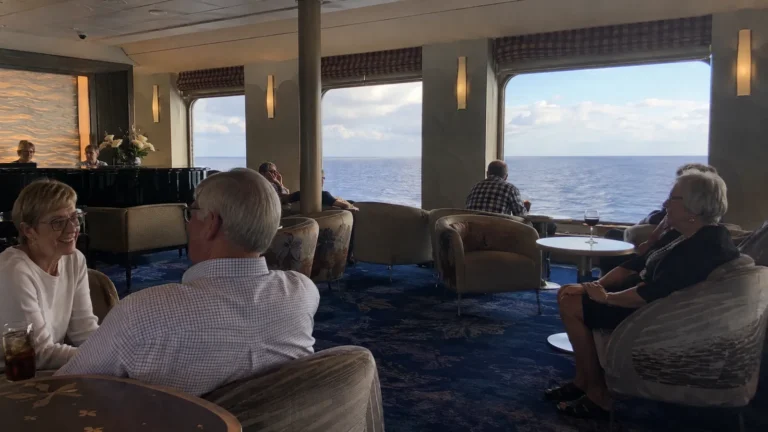 Passengers relaxing and chatting in an ocean-view ship lounge.