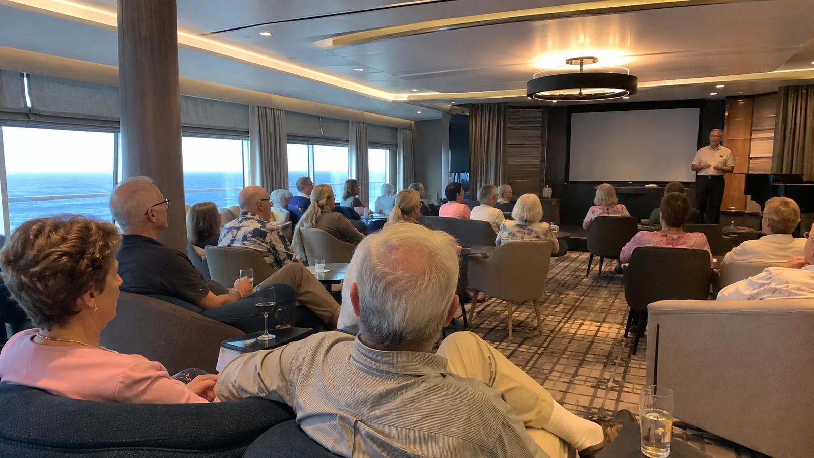 Passengers attending a talk in a shipboard lounge.