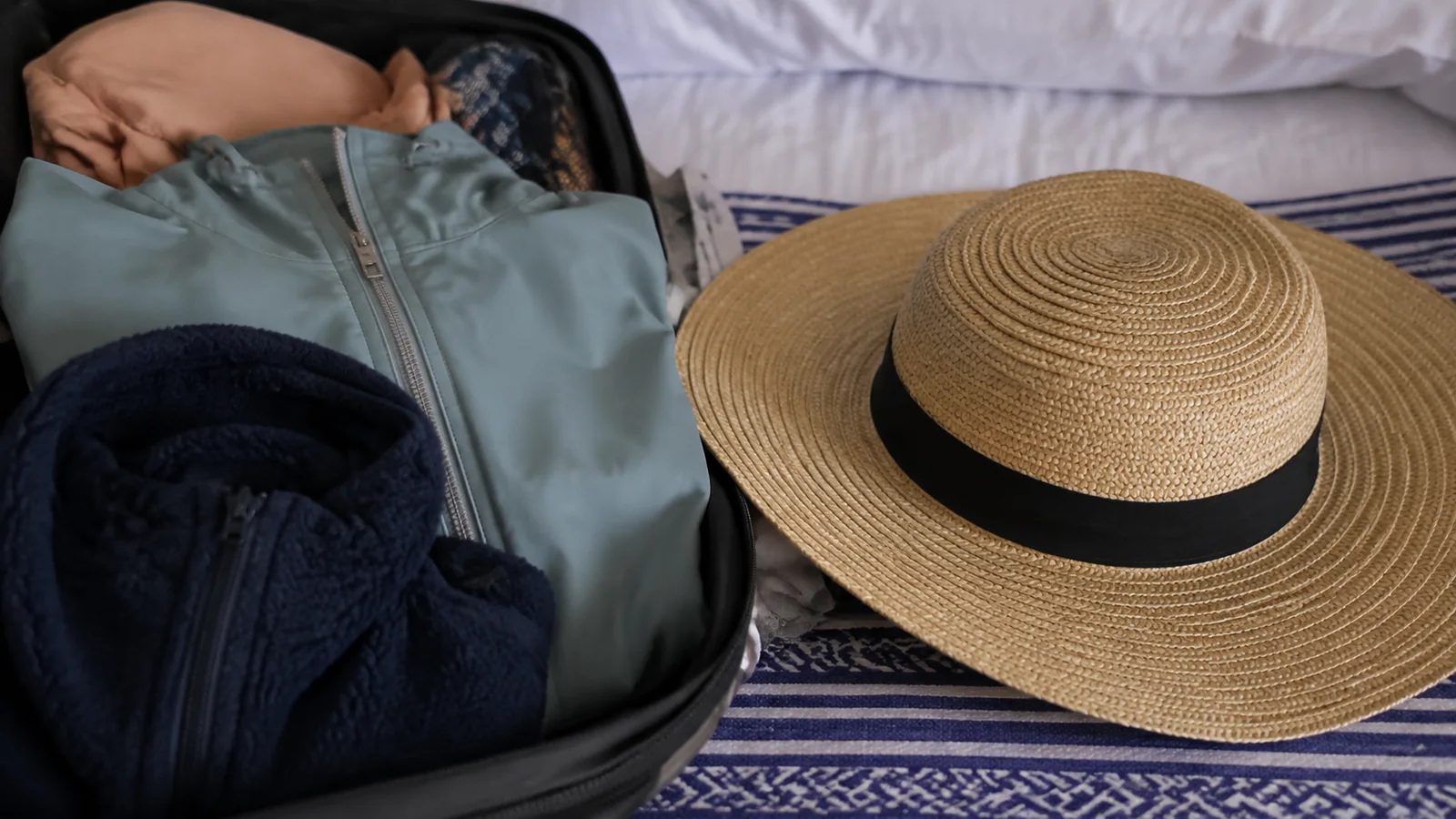 Sunhat beside warm and light clothing packed in a suitcase.