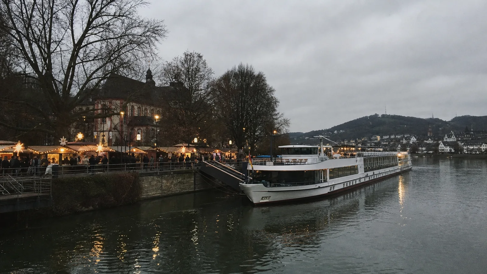 River cruise boat docked beside a waterfront decorated with festive lights.