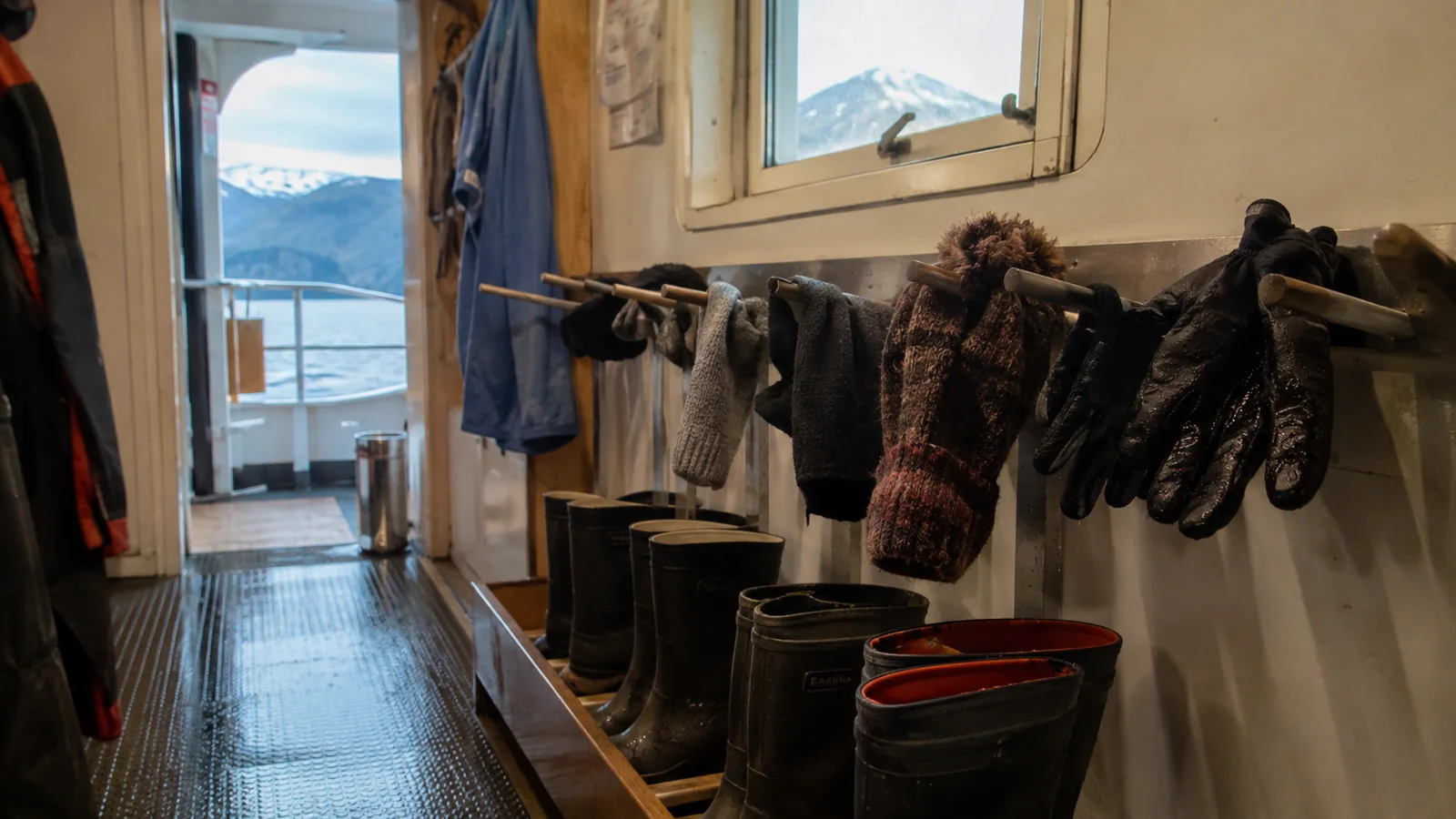 Gloves and outdoor clothing drying above rubber boots near a cabin doorway.