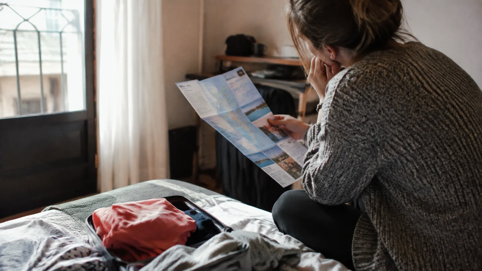 Traveler comparing a brochure with packed clothing on a bed.