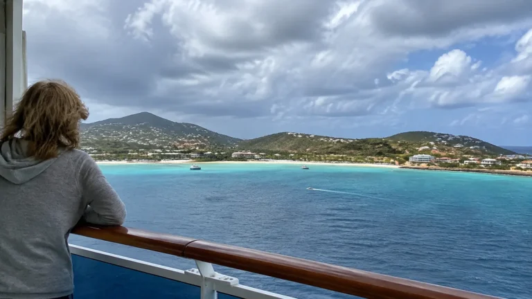 Passenger watching a turquoise bay from a cruise ship balcony.