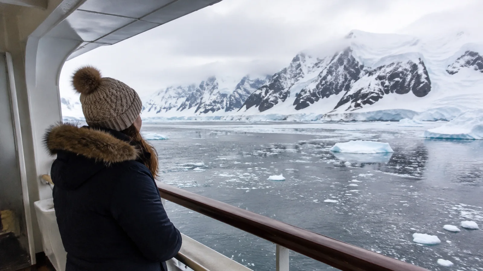 Traveler in a warm jacket viewing ice floes and snowy mountains from a ship.