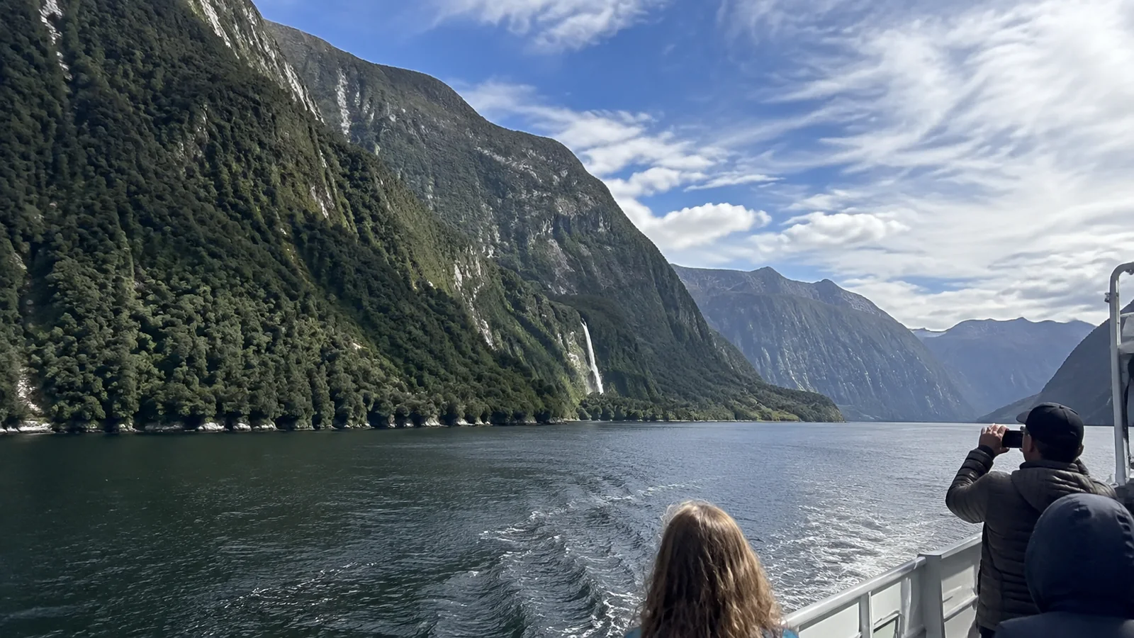 Passengers photographing a waterfall along a steep-sided fjord.