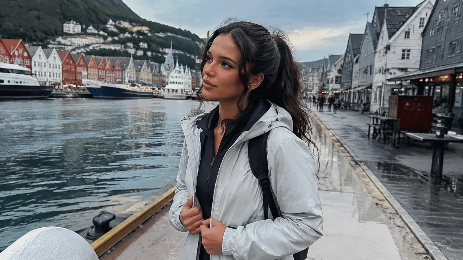 Woman in a rain jacket walking along a colorful waterfront.
