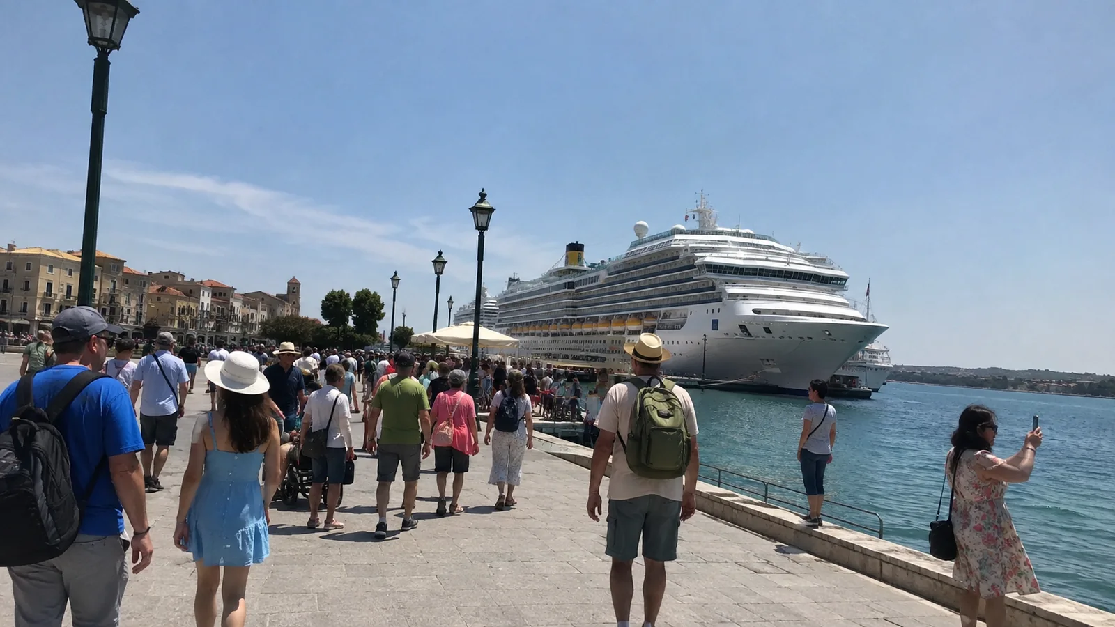 Crowds walking along a sunny waterfront toward a docked cruise ship.