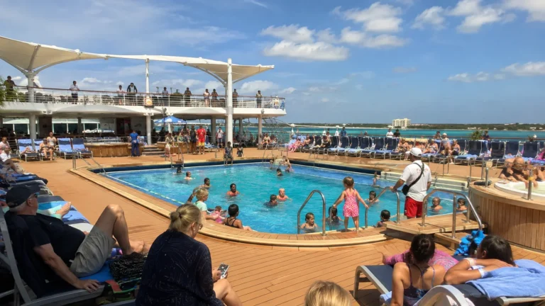 Busy outdoor cruise pool with passengers swimming and sunbathing.