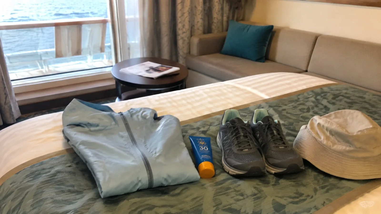 Light jacket, walking shoes, hat and sunscreen laid out on a cabin bed.