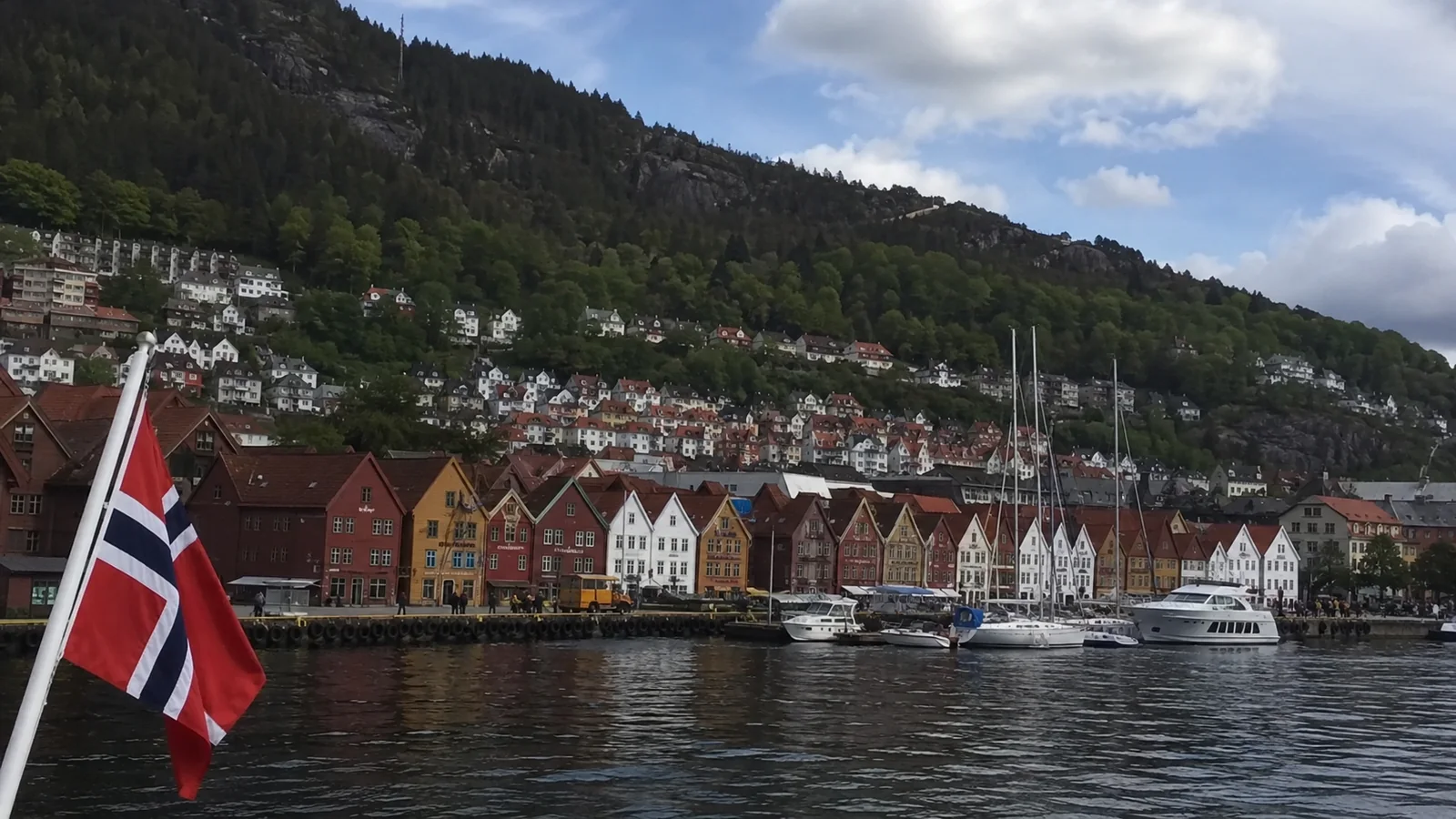 Colorful waterfront buildings viewed from a boat flying a Norwegian flag.