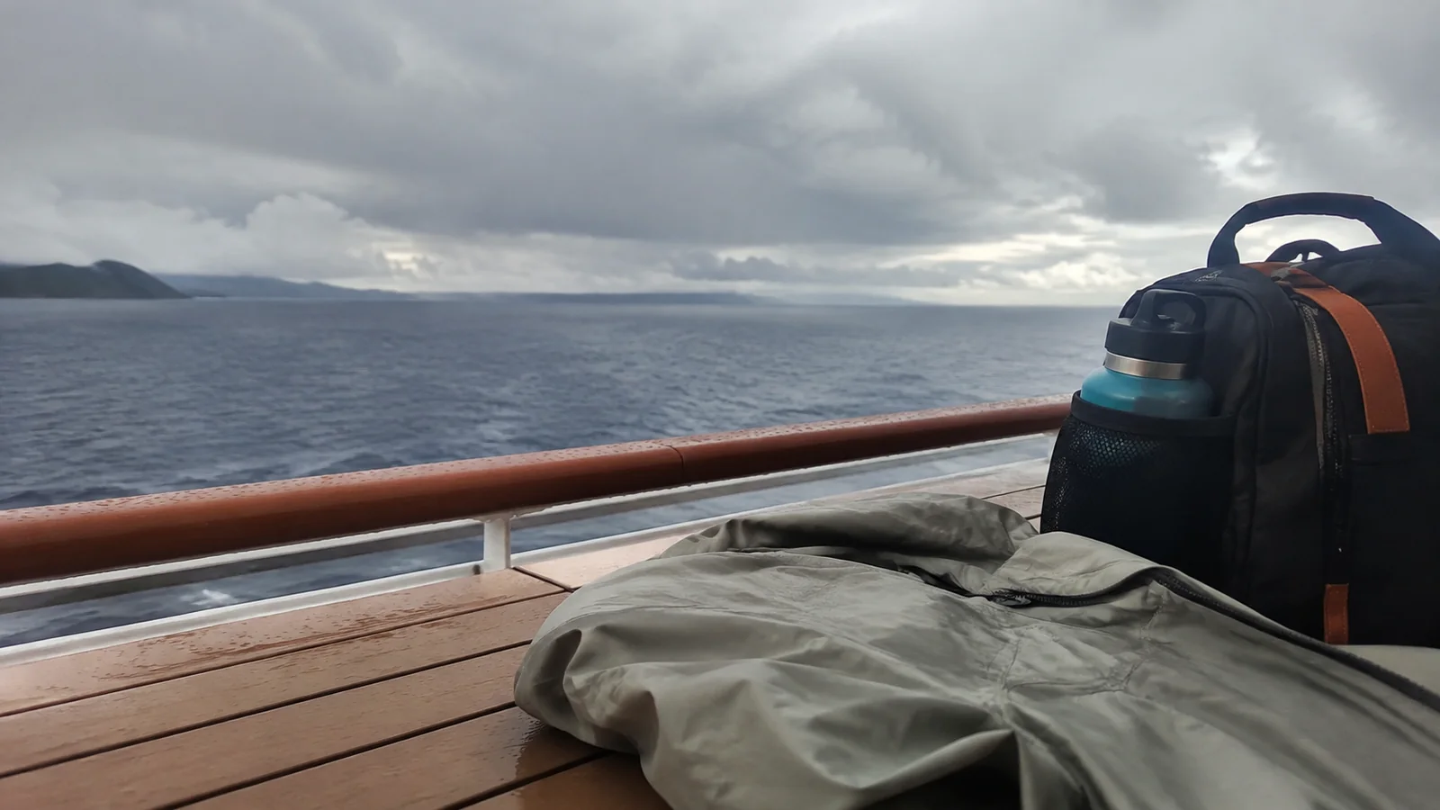 Rain jacket and backpack with a water bottle on a ship's outdoor table.