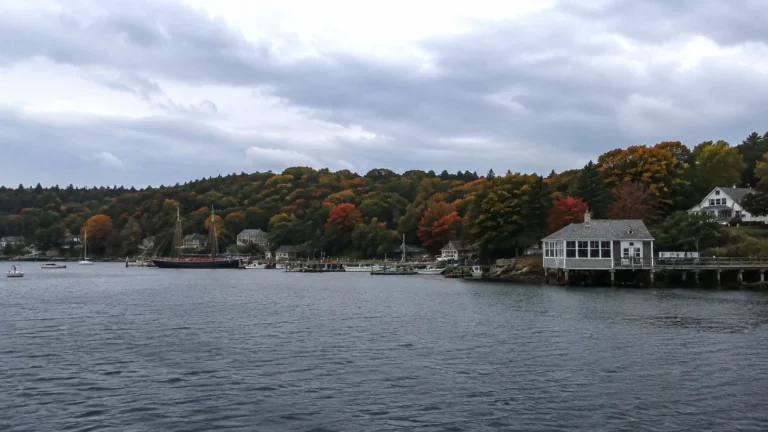 Waterfront houses backed by trees in orange and green autumn foliage.