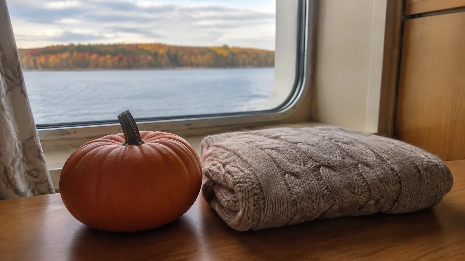 Small pumpkin and folded sweater beside a ship window.