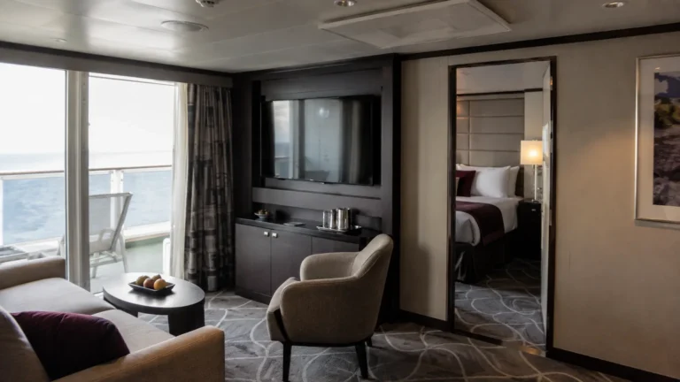 Cruise suite sitting room with a separate bedroom and ocean-facing balcony.