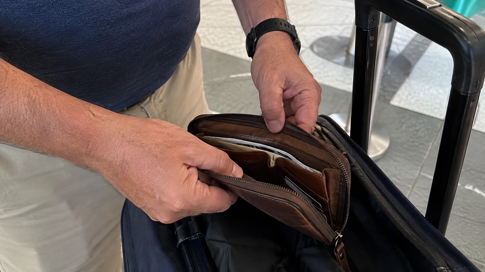 Traveler sorting documents in a zippered wallet beside a suitcase.