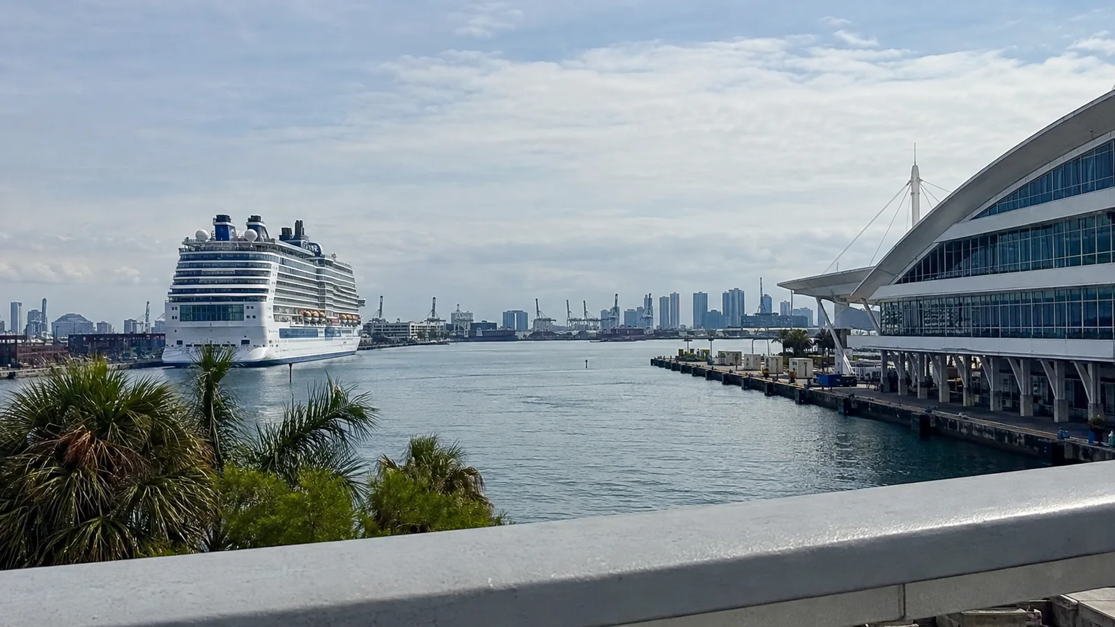 Cruise ship beside a modern terminal and harbor skyline.