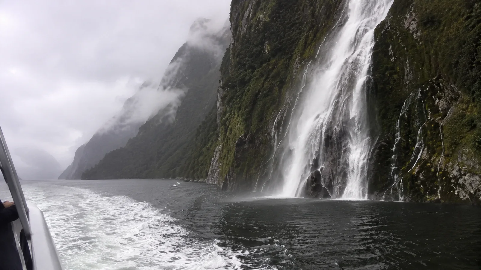 Waterfall plunging from a steep fjord cliff into dark water