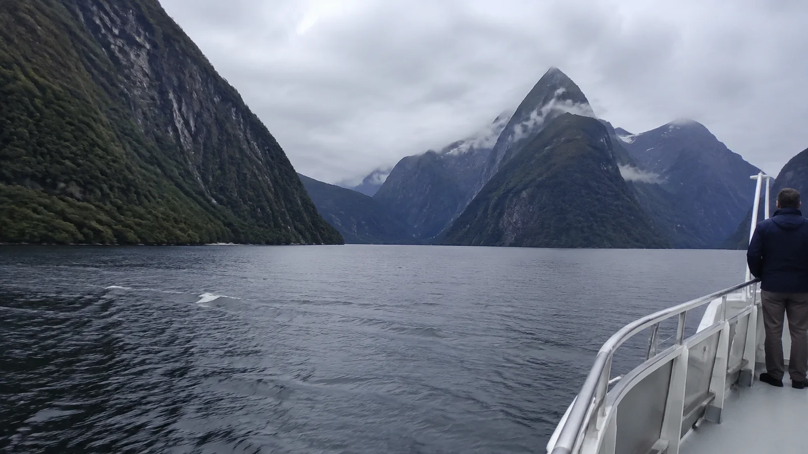 Boat deck moving through a fjord surrounded by steep mountains
