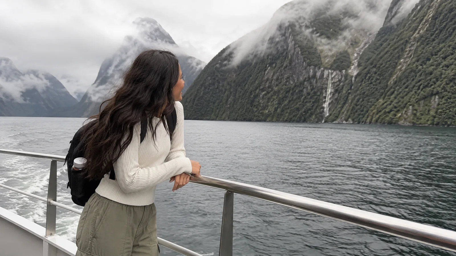 Woman at a railing looking toward a tall waterfall on a fjord cliff